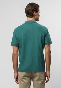 Tyrkysová polokošeľa s krátkym rukávom, golierom, štruktúrovanou tkaninou a bočnými rozparkami, skombinovaná s svetlými nohavicami.