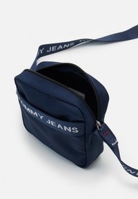 Bolso cruzado en color navy fabricado con un material duradero que cuenta con un cierre de cremallera, un bolsillo frontal y una correa ajustable con la marca "TOMMY JEANS".