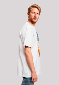 White cotton t-shirt featuring a multicolored geometric pattern on the front, short sleeves, and a relaxed fit. Slim, straight-cut jeans.