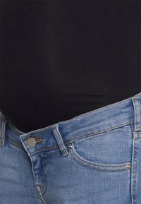 Body preto sobre calças de ganga de denim azul claro com um design clássico de cinco bolsos e com ilhoses prateados na cintura.