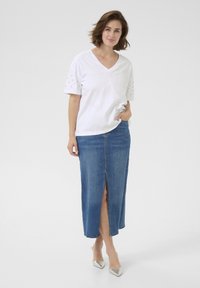 T-shirt blanc à col en V avec des manches courtes ornées, associé à une jupe en denim bleue avec une fente à l'avant. Talons argentés élégants.