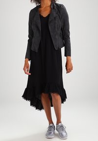 Musta midi-mekko, jossa on röyhelöhelma, yhdistettynä harmaaseen tekonahkamoottoripyörätakkiin ja hopeisiin urheilukenkään. Yksinkertainen muotoilu, sileä pinta.