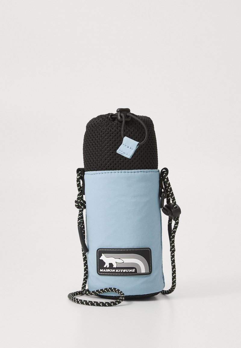 Saco cilíndrico azul claro com topo de malha preta, apresenta um patch decorativo com logo e alça ajustável. Tecido texturizado com materiais mistos.