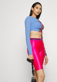 Modrý dlouhý rukáv crop top s našívkou a růžové vysoké cyklistické kraťasy s vzorovaným akcentem a černým pasem. Černá kabelka.