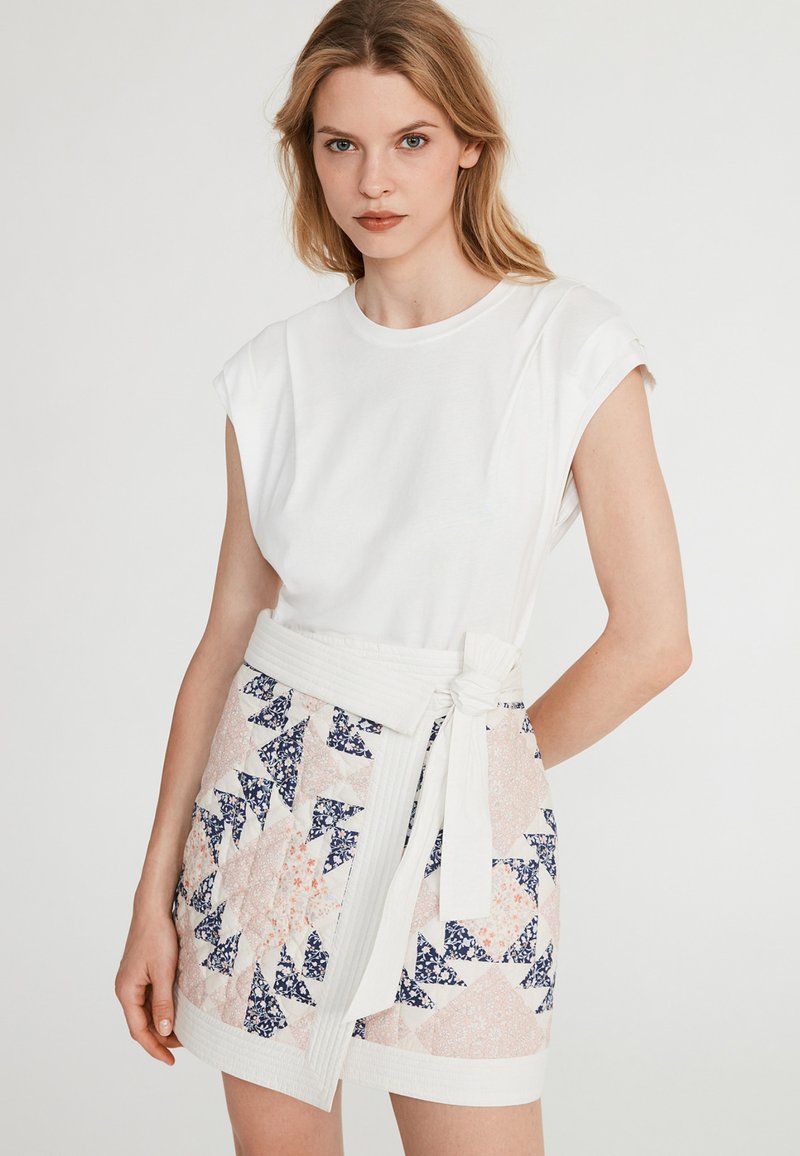 Witte top met korte mouwen, gecombineerd met een patroonrok met geometrische vormen in roze en marineblauw, met een strikceintuur in de taille.