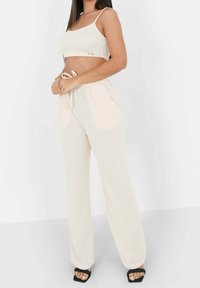 Crop top en tricot clair avec des bretelles fines et un pantalon à cordon assorti avec des poches latérales et une coupe décontractée. Des sandales noires complètent le look.