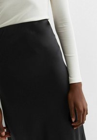 Falda de satén negra con una textura suave, combinada con una blusa de manga larga blanca con relieve, mano parcialmente visible sosteniendo la tela.