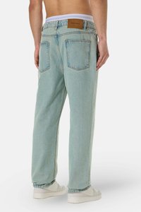 Light blue denim jeans with a relaxed fit, featuring a brown leather patch at the waistband and two back pockets. Combined with white sneakers.