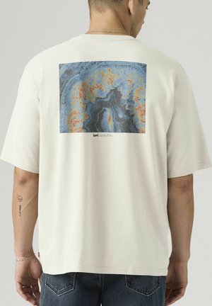 Homme portant un t-shirt blanc avec un imprimé géode bleu et orange et le logo Levi Strauss & Co. au dos, associé à un jean bleu foncé.
