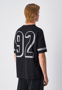 Camiseta de algodón negra con un gran estampado numérico gris "92" en la parte posterior, con mangas cortas y cuello redondo.