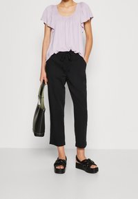 Haut court à manches courtes de couleur mauve clair avec des épaules froncées, associé à un pantalon noir à cordon de serrage. Présente une texture lisse et des sandales à plateforme noires.