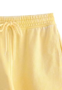 Pantaloni della tuta gialli in cotone con vita elastica e coulisse, caratterizzati da una texture morbida e un design semplice.