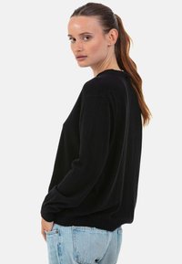 Pull noir en matière douce, coupe décontractée avec épaules tombantes et poignets côtelés, associé à un jean bleu clair.