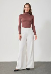 Coltrui in bordeauxrood, nauwsluitend silhouette; witte broek met wijde pijpen; strakke zwarte schoenen; gladde textuur overal.