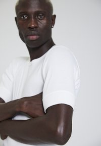 White cotton t-shirt with short sleeves, featuring a round neckline and a fitted shape. Smooth texture, minimal stitching details.