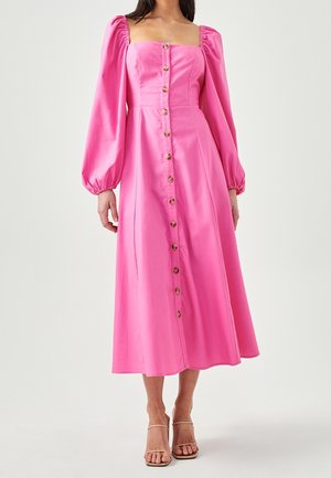 Donna che indossa un vestito midi rosa acceso con maniche lunghe a sbuffo, bottoni frontali, scollo quadrato e tacchi aperti beige.
