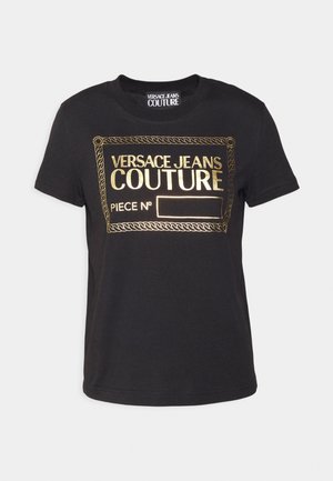 Camiseta negra de manga corta con el logo dorado "Versace Jeans Couture" y un marco rectangular decorativo en el frente.