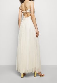 Bíl dress s délka až po zem, s průhlednou tylovou sukní, květinově vyšívaným korzetem a odhaleným zadním dílem. Má tenké ramínka a zúžený pas.