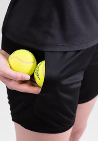 Pantaloni sportivi neri con una tasca laterale che tiene due palline da tennis gialle brillanti, realizzati in un tessuto liscio e leggero.