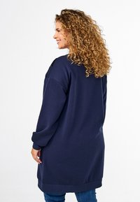 Felpa lunga blu navy con vestibilità rilassata, scollo rotondo e maniche lunghe. Accenti neri testurizzati sulle spalle. Materiale morbido in misto cotone.