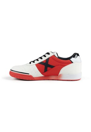 Chaussure de sport blanche et rouge avec des lacets noirs et un motif en X noir sur le côté, dotée d'une semelle rouge et d’un panneau rouge perforé.