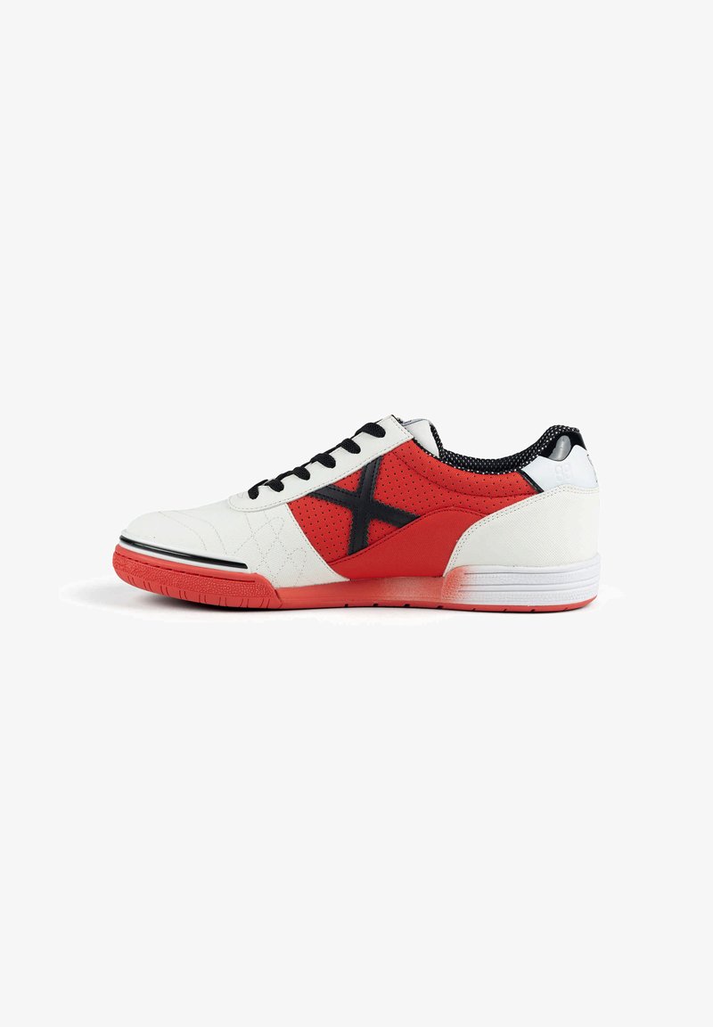 Chaussure de sport blanche et rouge avec des lacets noirs et un motif en X noir sur le côté, dotée d'une semelle rouge et d’un panneau rouge perforé.