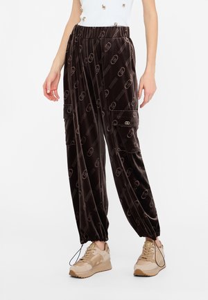 Pantaloni cargo in velluto marrone con un motivo a logo ripetuto, polsini elasticizzati, due tasche laterali e una vita con cordino, abbinati a sneaker beige.