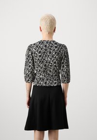 Angepasste Bluse mit schwarz-weißem Muster und Dreiviertelärmeln, kombiniert mit einem schwarzen, ausgestellten Rock, von hinten betrachtet.