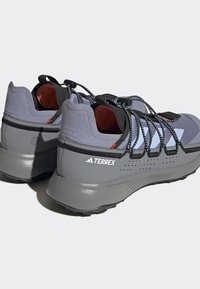 Tenis de desporto cinzentos com uma mistura de tecido texturizado e material sintético, apresentando pormenores pretos e um sistema de atacadores distintivo.