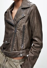 Bruine nepleer bikerjack met grote revers, meerdere ritsen en drukknoopdetails. Gekropt ontwerp, gestructureerd oppervlak.