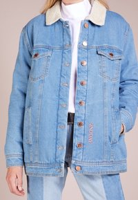 Ljusblå denimjacka med en krämfärgad fuskpälskrage. Har kopparfärgade knappar, två bröstfickor och broderad '2ND DAY' på sidan.