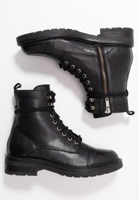 Botas ankle de cuero negro con un acabado texturizado, que presentan un sistema de cordones en la parte delantera, cremallera lateral y suela plana de goma. Diseño duradero con acentos metálicos.