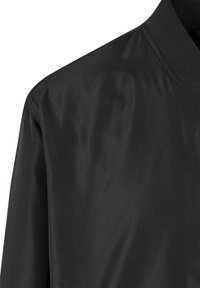Veste aviateur noire en tissu lisse et brillant, avec un col côtelé, au design épuré et minimaliste sans embellissements visibles.