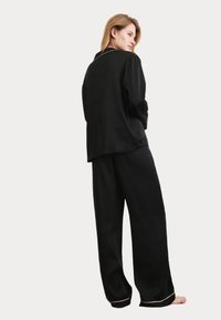 Svart silkespjälka set med en långärmad knäppning topp och vida byxor med kontrasterande piping längs kanterna. Mjuk textur, avslappnad passform.