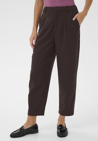 Dark brown high-waisted trousers with a pleated design, side pockets, and a tapered ankle. Worn with black loafers. Smooth fabric texture.