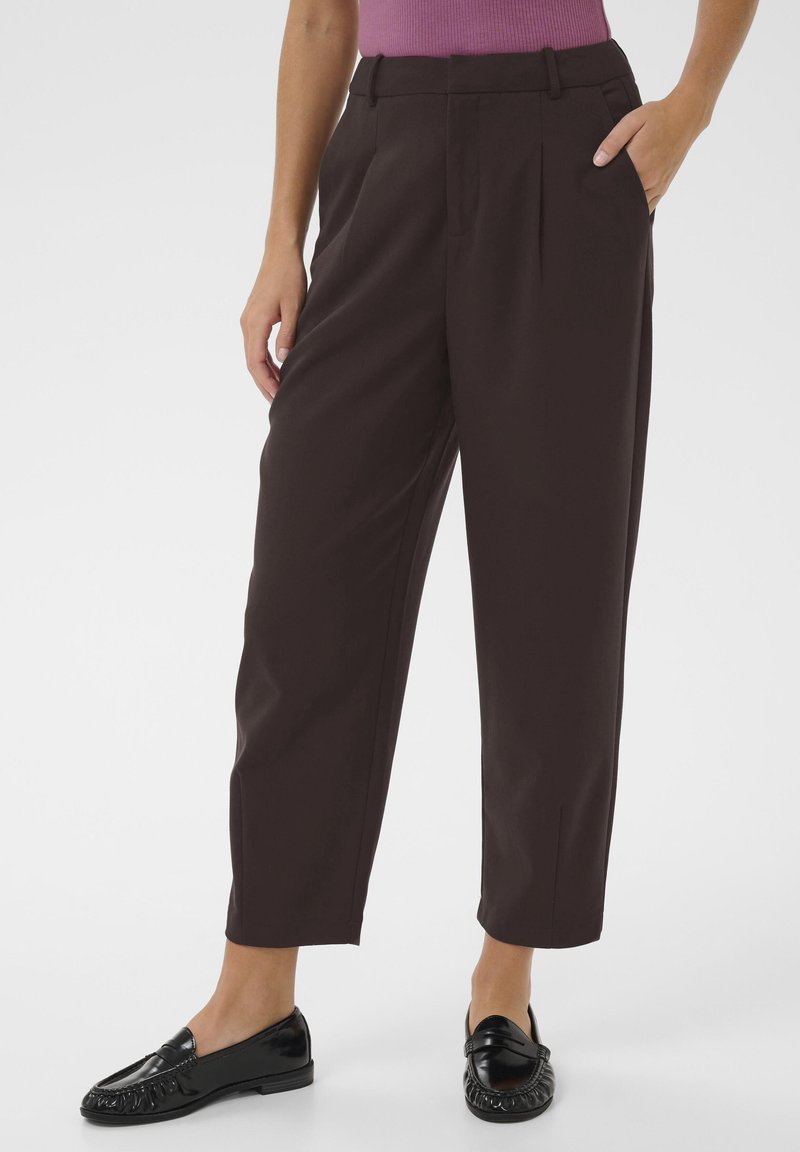Dark brown high-waisted trousers with a pleated design, side pockets, and a tapered ankle. Worn with black loafers. Smooth fabric texture.