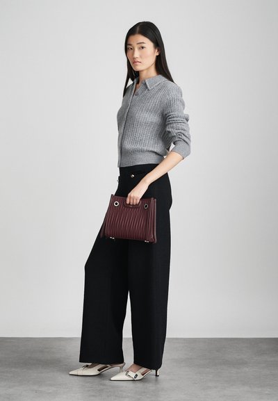 Grijze geribbelde cardigan met een kraag, gecombineerd met zwarte wijde broek. Burgondische handtas heeft verticale ribbels. Beige slingback schoenen maken de look compleet.