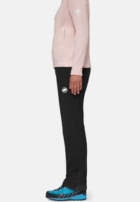 Czarne spodnie wędkarskie z bocznymi zamkami, w połączeniu z jasnoróżową bluzą z długim rękawem i niebieskimi butami wędkarskimi z czarnymi akcentami.