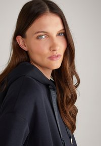 Felpa con cappuccio navy dalla vestibilità rilassata, caratterizzata da una chiusura con cordoncino con punte metalliche e un tessuto morbido e strutturato.