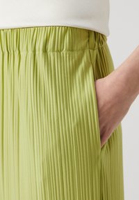 Faltenformikierte grüne Hose mit elastischem Bund und Seitentaschen, die eine glatte Textur und einen leichten Stoff aufweist.