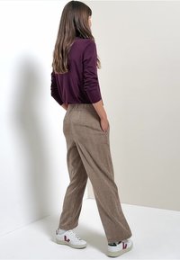 Bruna kordflöjtsbyxor med avslappnad passform och elastiskt midjeband, tillsammans med en mörklila långärmad topp och vita sneakers.