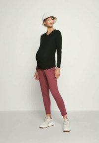 Μαύρη μπλούζα με μακριά μανίκια, ροζ εφαρμοστά παντελόνια, άσπρο καπέλο τύπου bucket και άσπρα αθλητικά παπούτσια. Διαθέτει κυματιστό στρίφωμα στην μπλούζα. Λείο υφασμάτινο σχέδιο.