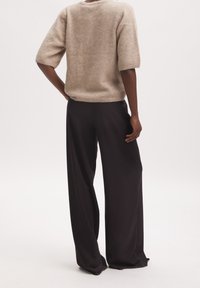 Beige, kurzärmliger, flauschiger Strickpullover kombiniert mit schwarzen, weiten Hosen. Weiche Textur, lockere Passform und minimalistisches Design.