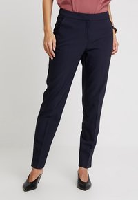 Marinblå stretchbyxor med smalben, med framfickor och en slät yta. Kombinationen med en rosafärgad topp och svarta klackar.