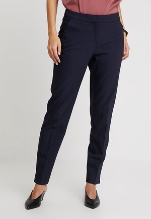 Navy stretchbroek met een tapse pijp, voorzien van zijzakken en een gladde afwerking. Gepaard met een rozenkleurige top en zwarte hakken.