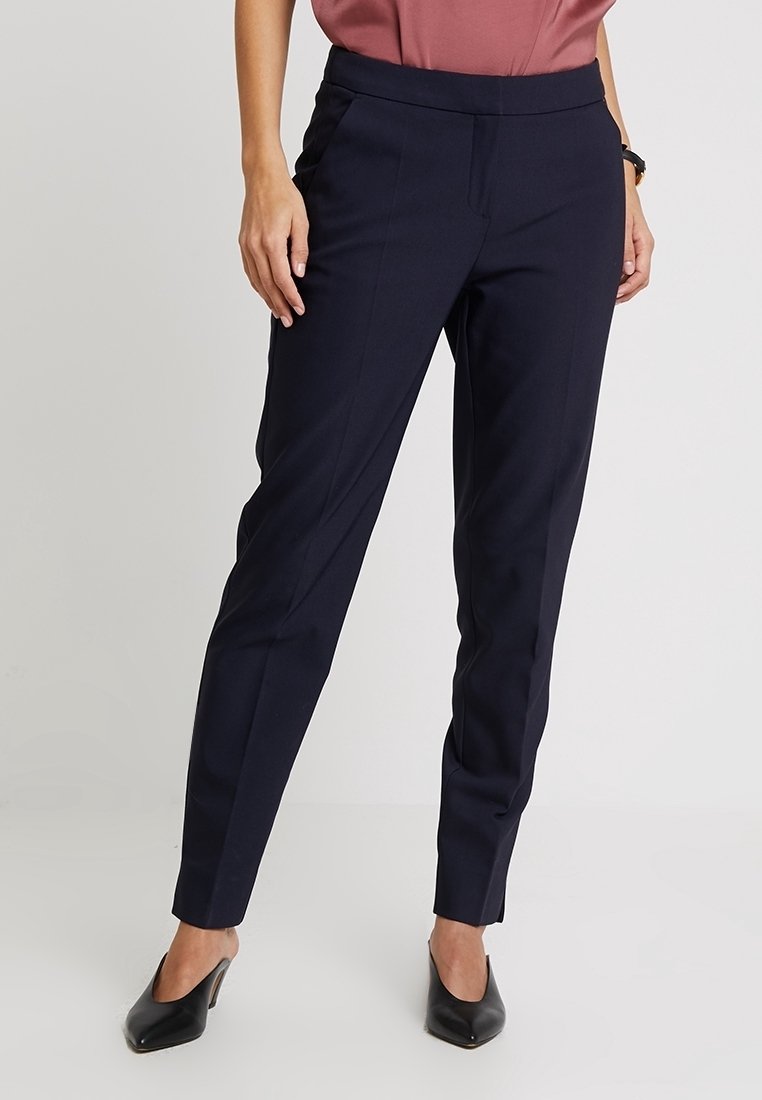 Marinblå stretchbyxor med smalben, med framfickor och en slät yta. Kombinationen med en rosafärgad topp och svarta klackar.