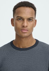 Tengerészeti textúrájú kötött pulóver kerek nyakkal. Egyenletes mintázattal és bordázott nyakkal rendelkezik. A modellen rövid, göndör haj van.