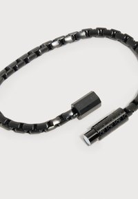 Μαύρο βραχιόλι αλυσίδα από μέταλλο με ορθογώνιους κρίκους και κυλινδρικό κούμπωμα χαραγμένο με το λογότυπο Calvin Klein σε λευκό φόντο.