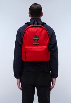 Zaino di stoffa rosso con un logo rotondo, tasca frontale con zip e spallacci regolabili. Texture liscia e forma strutturata.