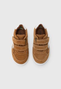 Baskets en daim marron avec accents blancs, deux sangles Velcro, détails perforés et une languette en maille texturée. Bout arrondi et semelle en caoutchouc.